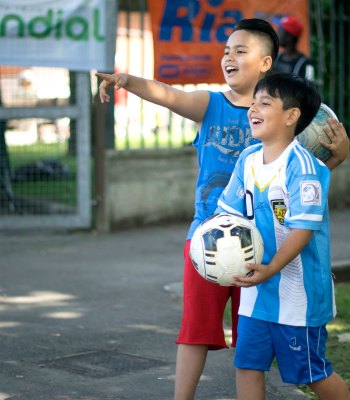 Two kids smiling and playing football.